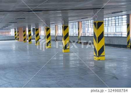 An expansive parking garage features yellow and black safety barriers on the columns, illuminated by natural light from large windows 124988784