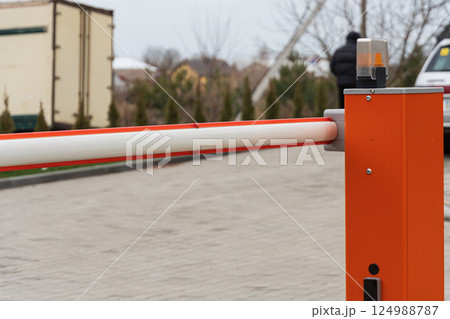 Barrier gate stands at a parking entrance, illuminated by a lamp, as a vehicle approaches on a cloudy day, surrounded by greenery Barrier gate stands at a parking entrance, illuminated by a lamp, as a vehicle approaches on a cloudy day, surrounded by greenery 124988787