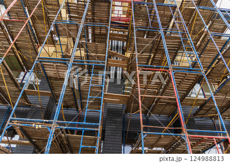 Workers utilize colorful scaffolding to access upper levels of a building under renovation in an urban area during daylight 124988813