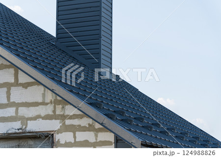 A detailed view of a recently installed metal roof on a house emphasizing the chimney and surrounding construction elements 124988826