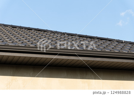 Textured roofing material on a modern home reflects sunlight under a clear blue sky, showcasing craftsmanship and design elements 124988828