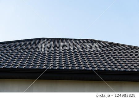 A black tile roof showcases its neat pattern under a clear blue sky, emphasizing craftsmanship and modern architectural design 124988829