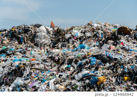 Piles of plastic, paper, and other waste dominate the landscape at a landfill site on a sunny day in an urban area 124988942