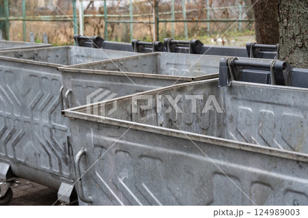 Metal containers stand empty and unused in a recycling area, capturing the quiet moment in an urban landscape on an overcast day Metal containers stand empty and unused in a recycling area, capturing the quiet moment in an urban landscape on an overcast day 124989003
