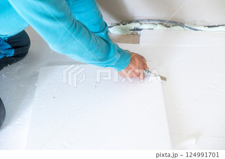 Construction worker cutting styrofoam insulation board with utility knife Construction worker cutting styrofoam insulation board with utility knife 124991701