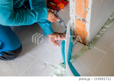Construction worker is cutting edge insulation panel using utility knife during floor installation 124991712