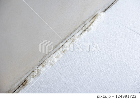 Construction worker applying polyurethane expanding foam insulation to floor and wall joint 124991722