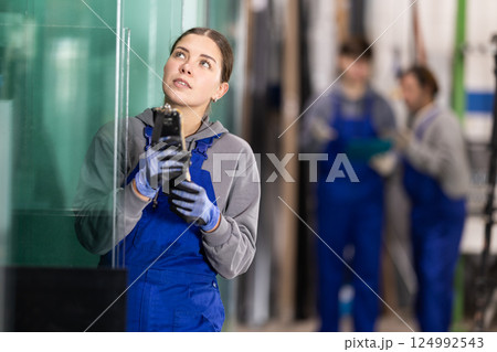 Young woman employee in blue overall uses remote control to move lifting mechanism Young woman employee in blue overall uses remote control to move lifting mechanism 124992543