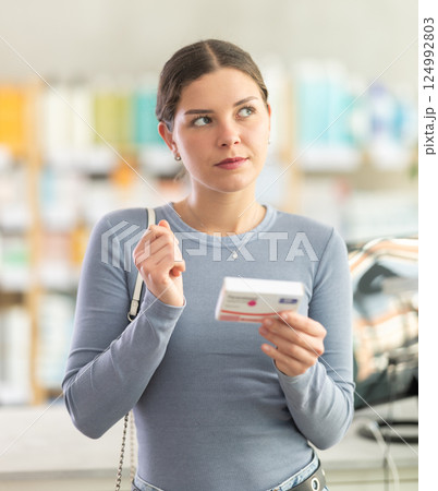 Young woman choosing pain or fever relief medicine in pharmacy 124992803