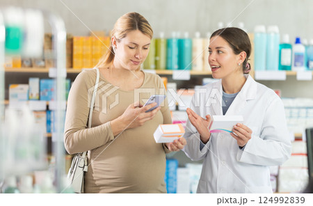 Expecting woman comparing supplements using phone at drugstore 124992839