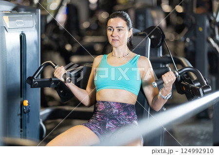 In gym, woman uses chest press machine to strengthen arm muscles In gym, woman uses chest press machine to strengthen arm muscles 124992910