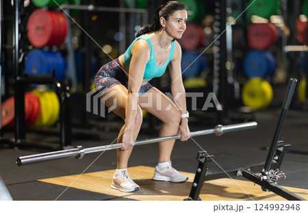 Woman trains muscles of arms, standing up doing barbell exercises Woman trains muscles of arms, standing up doing barbell exercises 124992948