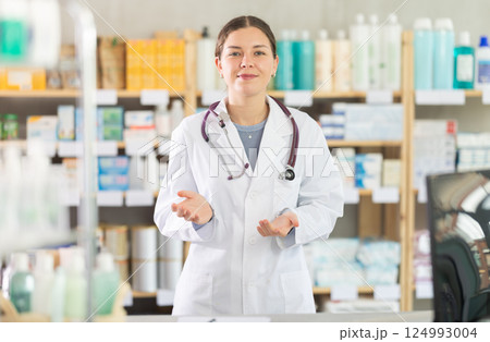 Smiling young female pharmacist inviting for consultation at drugstore Smiling young female pharmacist inviting for consultation at drugstore 124993004