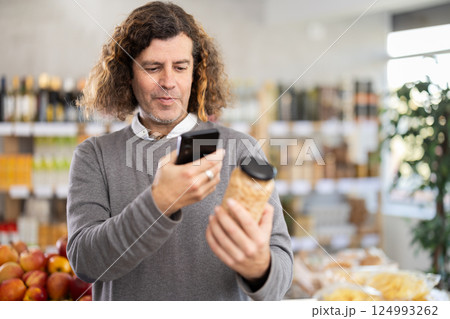 Checking expiration date of beans - male shopper scans QR code on label of jar canned beans using smartphone 124993262