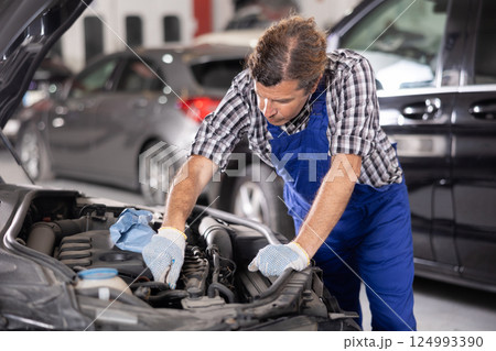 Experienced auto mechanic repairing car engine in workshop Experienced auto mechanic repairing car engine in workshop 124993390