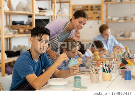 Teenage boy painting ceramic cupin pottery workshop 124993417