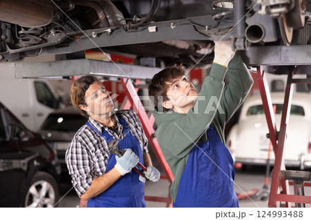 Auto repair shop owner inspecting car on lift with young mechanic Auto repair shop owner inspecting car on lift with young mechanic 124993488