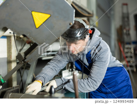 Young guy puts steel part on machine Young guy puts steel part on machine 124993489