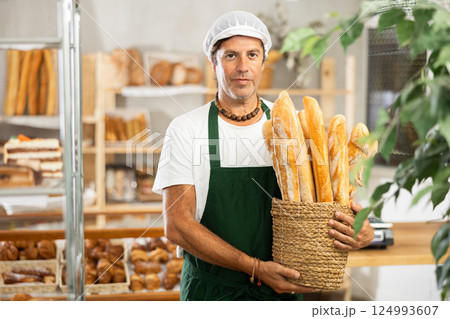 Middle-aged salesman holding baguettes in wicker basket Middle-aged salesman holding baguettes in wicker basket 124993607