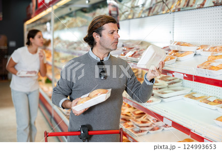 Attentive customer chooses chicken meat in the meat department of supermarket 124993653