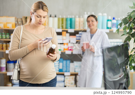 Pregnant woman in pharmacy scan QR code on syrup, pharmacist offer similar product in background Pregnant woman in pharmacy scan QR code on syrup, pharmacist offer similar product in background 124993790