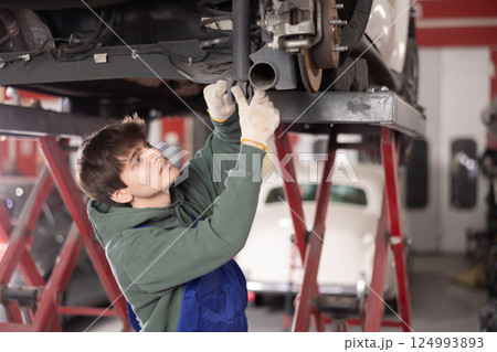 Young guy mechanic repairs underbody of car 124993893