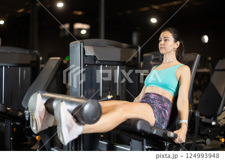 Woman working out on leg extension machine in gym 124993948