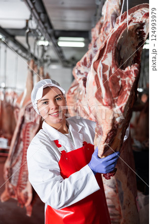 Female butchery worker checking hanging raw cow carcasses 124993979