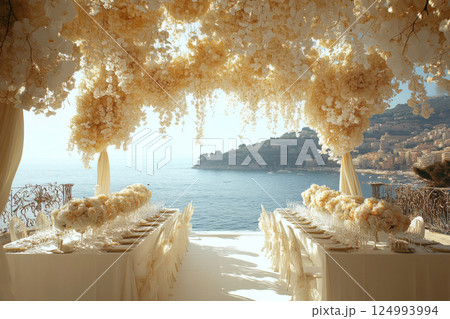 Beautiful wedding reception with long table of white flowers and tablecloths. Set up on beach with view of the ocean 124993994