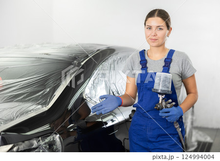 Young woman mechanic paints car with machine Young woman mechanic paints car with machine 124994004