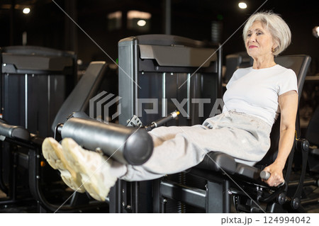 Elderly woman performing leg extensions on gym machine Elderly woman performing leg extensions on gym machine 124994042