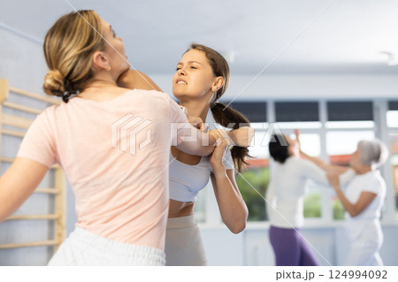 Woman and girl in gym perform basic elements of krav maga self-defense system. 124994092
