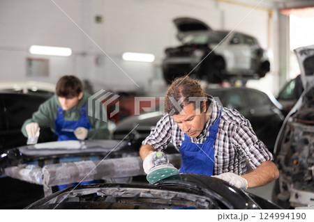 Adult male mechanic polishes car with machine Adult male mechanic polishes car with machine 124994190