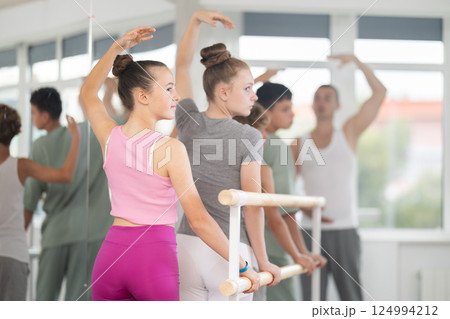 Girls and boys in ballet class perform third position under male teacher guidance. 124994212