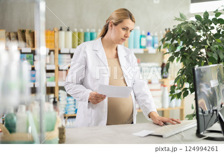 Pregnant pharmacist working with computer in chemist's shop 124994261