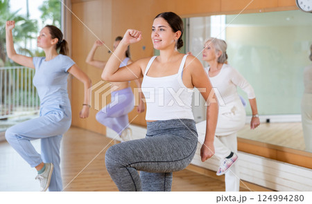 Group of excited young adult women in activewear performing dynamic movements during exercising together in fitness studio Group of excited young adult women in activewear performing dynamic movements during exercising together in fitness studio 124994280