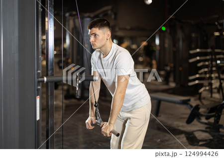 Young man training triceps on cable machine at gym 124994426