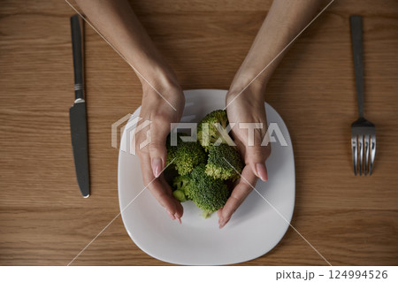 Female hands holding broccoli on the plate at home kitchen Female hands holding broccoli on the plate at home kitchen 124994526