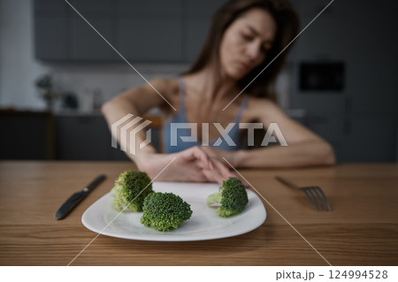 Skinny woman feeling nausea refusing to eat broccoli portion pushing plate away 124994528