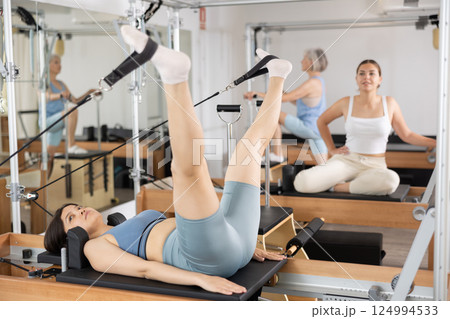 Positive woman practicing pilates stretching exercises on reformer at gym 124994533