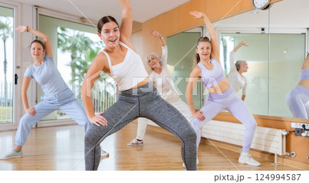 Ordinary active females exercising dance moves in modern dance studio Ordinary active females exercising dance moves in modern dance studio 124994587