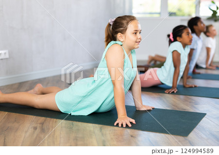 Children practicing yoga positions during group training in fitness center, performing stretching asana Urdhva Shvanasana Children practicing yoga positions during group training in fitness center, performing stretching asana Urdhva Shvanasana 124994589