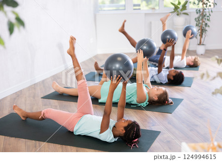Portrait of childrens with pilates balls, pumping press during group class in fitness studio 124994615
