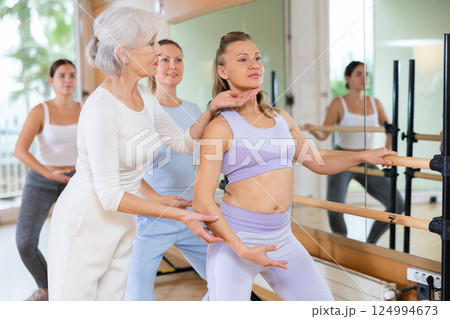 Elderly female choreographer adjusting head position of young woman near barre during class in dance school Elderly female choreographer adjusting head position of young woman near barre during class in dance school 124994673