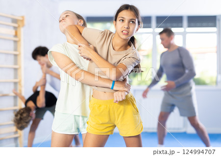 Two preteen girls train in pairs at self-defense lesson under guidance of trainer in gym 124994707
