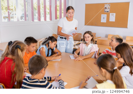 Teacher, together with group of schoolchildren, are looking for solution to complex tasck at round table in school classroom Teacher, together with group of schoolchildren, are looking for solution to complex tasck at round table in school classroom 124994746