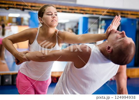 Girl practicing palm to launch blow in chin to man in training room Girl practicing palm to launch blow in chin to man in training room 124994938