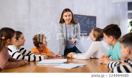 Positive female teacher explaining topic to tweens children during lesson in class of middle school Positive female teacher explaining topic to tweens children during lesson in class of middle school 124994980