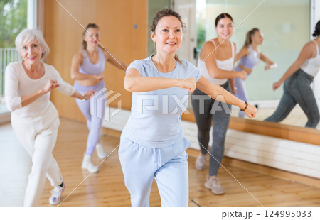 Excited positive women of different ages performing modern dancing exercises in school for adults Excited positive women of different ages performing modern dancing exercises in school for adults 124995033