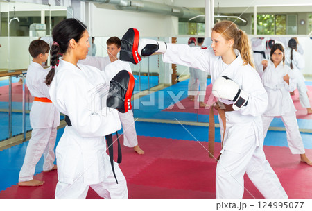 Female trainer in boxing gloves conducts sparring and teaches punches to girl in karate and self-defense training 124995077